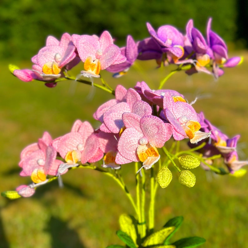 May include: A bouquet of pink and purple orchids with yellow centers. The orchids are arranged in a vase and have green stems and leaves.