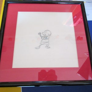 Puede incluir: Boceto de dibujos animados enmarcado de un personaje en posición de combate. La obra de arte está centrada en un fondo blanco, rodeada por un passe-partout rojo y encerrada en un marco negro. El marco es rectangular.