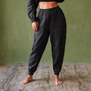 May include: Black linen crop hoodie and matching cargo pants. The hoodie has a front pocket and long sleeves. The pants have cargo pockets and elastic cuffs. The outfit is worn by a person in front of a green wall.