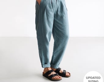 Puede incluir: Una persona con una camisa de lino beige claro y pantalones plisados ​​azul verdoso. La persona también lleva sandalias negras. La imagen incluye un círculo blanco con el texto "UPDATED SIZING CHART*".