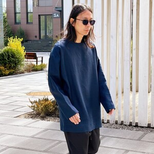 May include: A person wearing a dark blue long-sleeved shirt and black pants. The person is wearing sunglasses and walking outside.