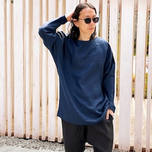 May include: A person wearing a dark blue long-sleeved shirt and black pants. The person is standing in front of a wooden slat wall.
