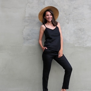 Puede incluir: Una mujer con un top de tirantes de lino negro y pantalones a juego. Lleva un sombrero de paja y sandalias.