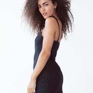 May include: A woman with curly brown hair wearing a black sleeveless dress.