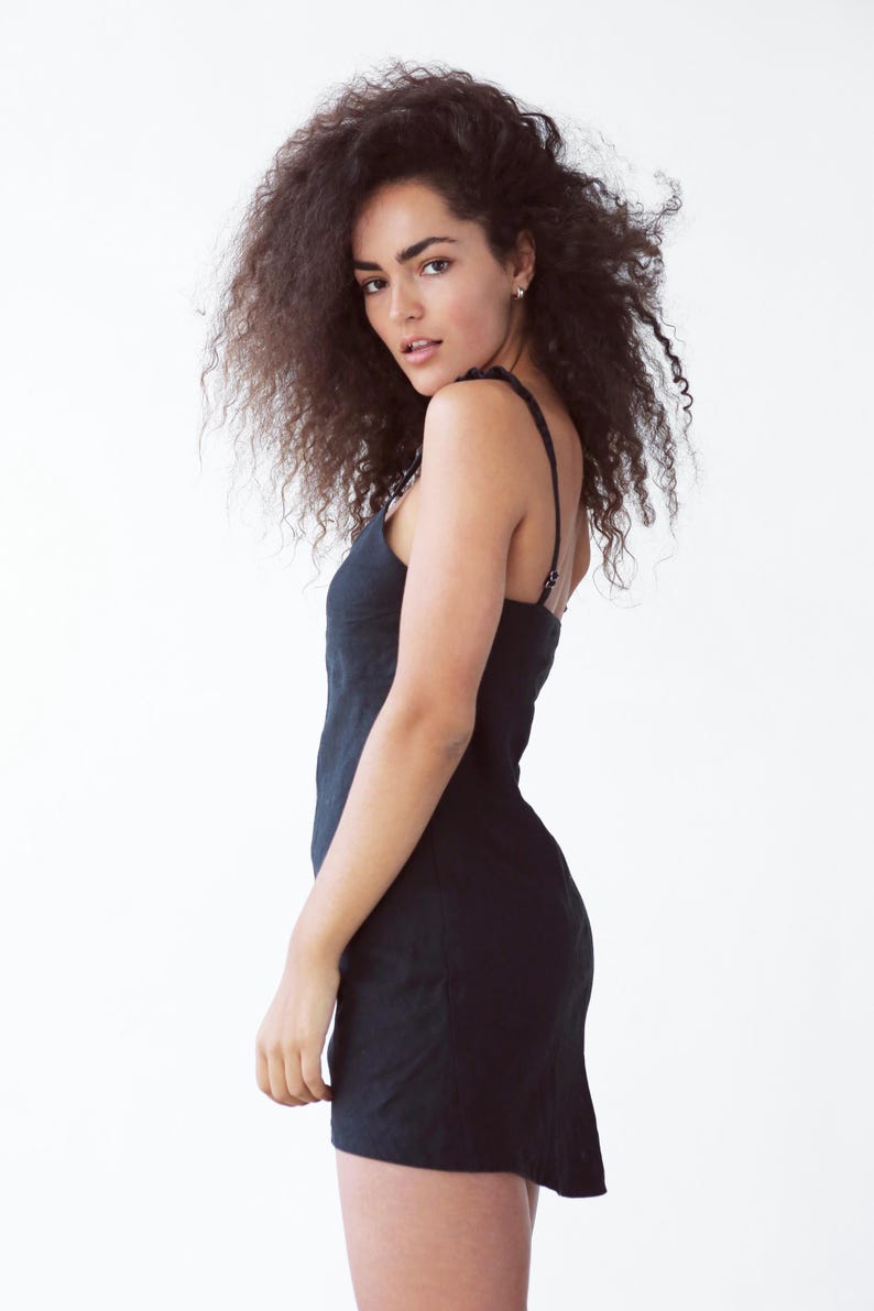 May include: A woman with curly brown hair wearing a black sleeveless dress.