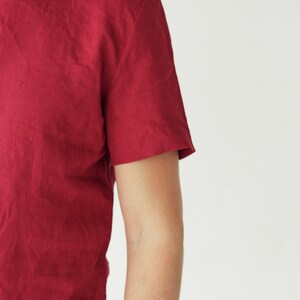 May include: A close-up of a red short-sleeved t-shirt made of a textured fabric. The shirt has a round neckline.