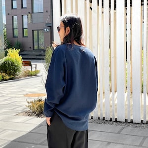 May include: A person wearing a dark blue long-sleeved shirt with a relaxed fit. The shirt has a round neckline and is made of a soft, comfortable fabric.