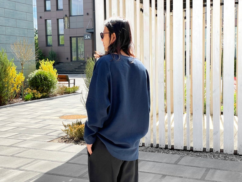 May include: A person wearing a dark blue long-sleeved shirt with a relaxed fit. The shirt has a round neckline and is made of a soft, comfortable fabric.