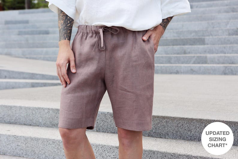 Pu&ograve; includere: Pantaloncini in lino color malva con vita con coulisse e tasche. I pantaloncini sono al ginocchio e abbinati a un top bianco. L'immagine include un piccolo cerchio bianco con la scritta "UPDATED SIZING CHART*"