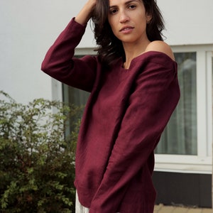 May include: A maroon linen top with long sleeves and a slightly off-the-shoulder neckline.