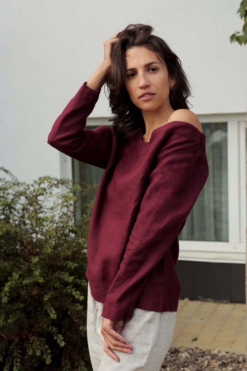 May include: A maroon linen top with long sleeves and a slightly off-the-shoulder neckline.
