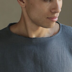May include: A close-up of a man wearing a dark gray linen shirt with a raw edge neckline.