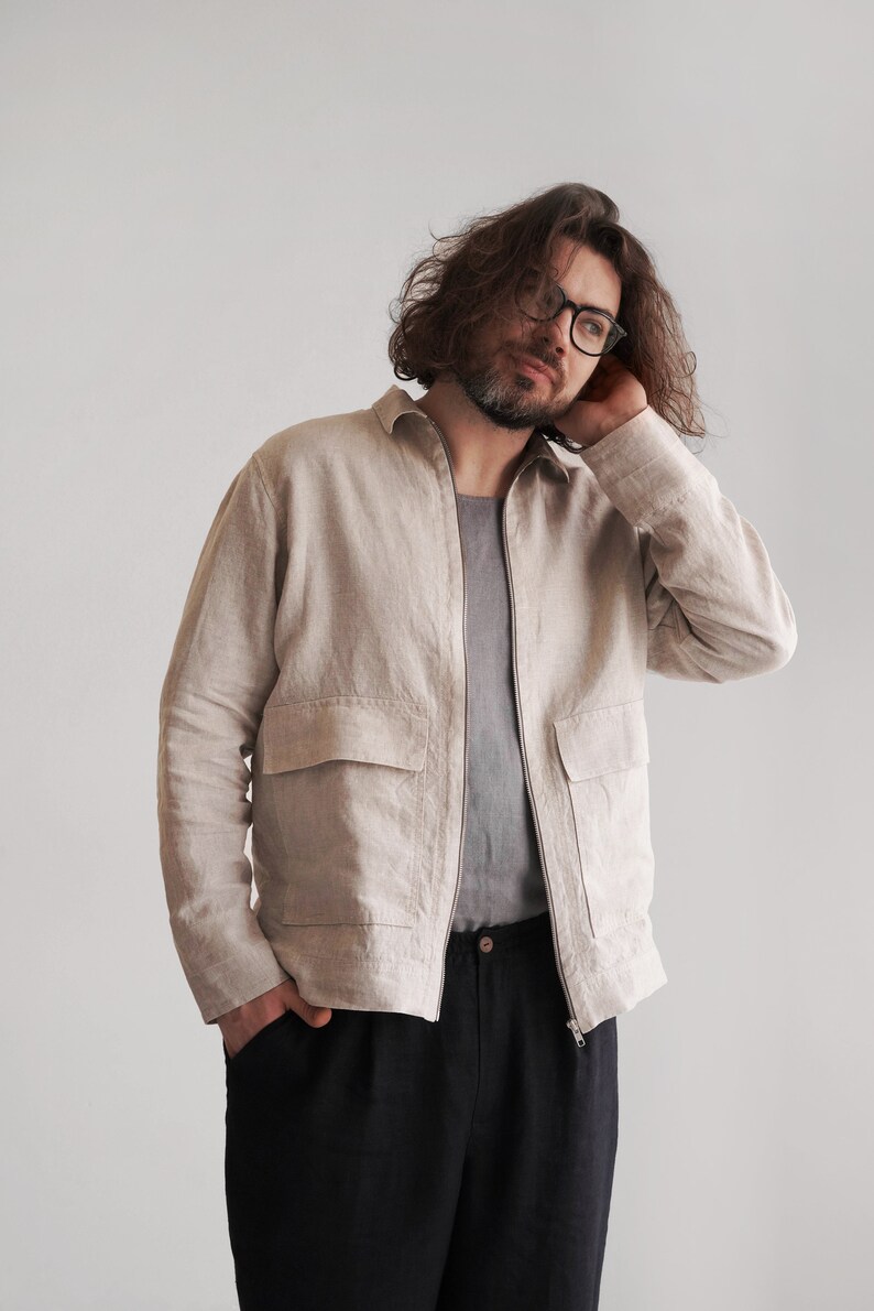 Puede incluir: Un hombre con una chaqueta de lino beige claro con cierre de cremallera y dos bolsillos grandes. Tambi&eacute;n lleva pantalones negros.