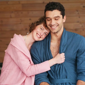Pode incluir: Um casal em um abra&ccedil;o amoroso, vestindo roup&otilde;es combinando azul e rosa. A mulher est&aacute; com a cabe&ccedil;a apoiada no ombro do homem, e ambos est&atilde;o sorrindo.