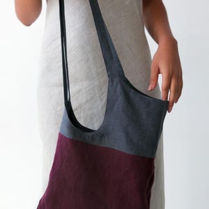 May include: A two-toned tote bag with a dark grey top section and a burgundy bottom section. The bag has a single strap and is made of a linen fabric.