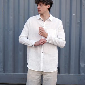 Pu&ograve; includere: Una camicia di lino bianca a maniche lunghe e colletto abbottonato. La camicia ha una tasca sul lato sinistro ed &egrave; indossata con pantaloni di lino beige.