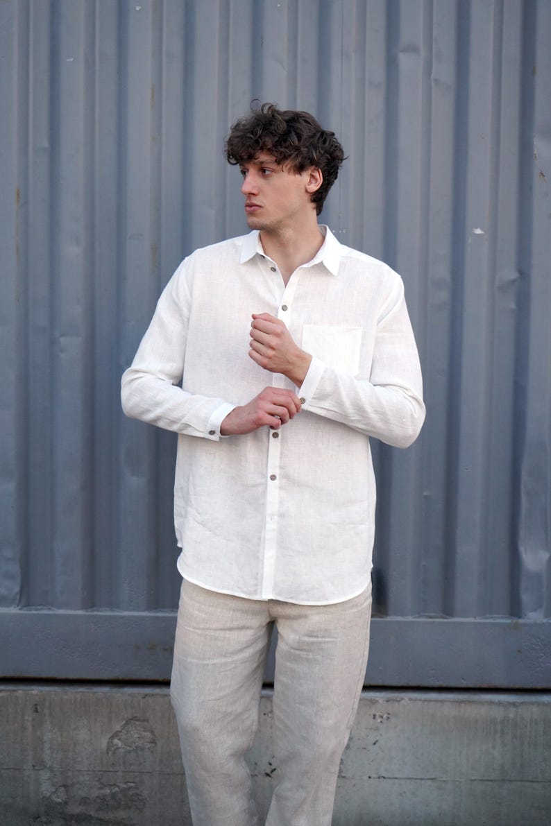 Pu&ograve; includere: Una camicia di lino bianca a maniche lunghe e colletto abbottonato. La camicia ha una tasca sul lato sinistro ed &egrave; indossata con pantaloni di lino beige.