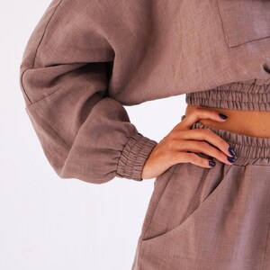 May include: A brown linen two-piece set with a cropped top and pants. The top has a relaxed fit with long sleeves and a drawstring waist. The pants have a relaxed fit with pockets and a drawstring waist.