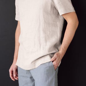 May include: A light beige linen t-shirt with short sleeves. The t-shirt is loose fitting and has a relaxed silhouette.