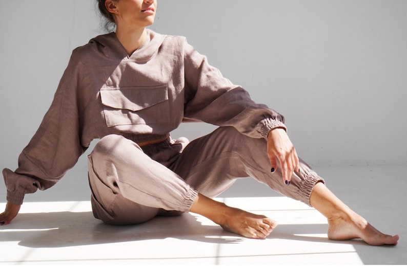May include: A mauve-colored linen hoodie and matching pants. The hoodie has a large pocket on the front and a drawstring hood. The pants have an elastic waistband and cuffed legs.