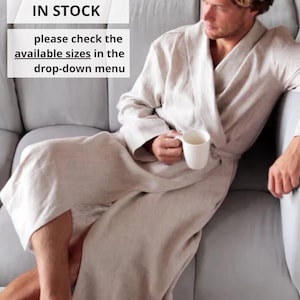 May include: A light beige linen robe with a matching belt. The robe is worn by a person sitting on a gray sofa and holding a white mug. Text on the image reads "IN STOCK" and "please check the available sizes in the drop-down menu."