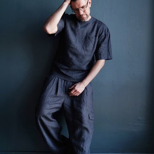 Pu&ograve; includere: T-shirt in lino grigio scuro con taschino sul petto e pantaloni cargo ampi abbinati. L'outfit &egrave; realizzato in un tessuto morbido e traspirante. Il modello indossa occhiali e scarpe da ginnastica.