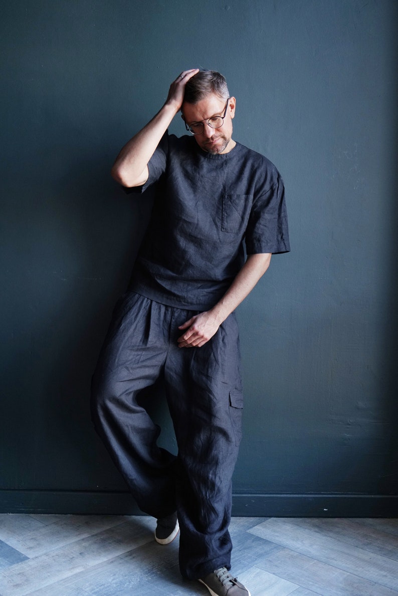 Pu&ograve; includere: T-shirt in lino grigio scuro con taschino sul petto e pantaloni cargo ampi abbinati. L'outfit &egrave; realizzato in un tessuto morbido e traspirante. Il modello indossa occhiali e scarpe da ginnastica.