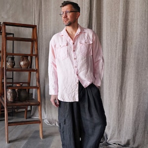 Pu&ograve; includere: Una camicia di lino rosa chiaro con due tasche sul petto e pantaloni cargo grigio scuro. La camicia ha una chiusura con bottoni e maniche lunghe. I pantaloni hanno grandi tasche laterali. L'outfit &egrave; casual e confortevole.