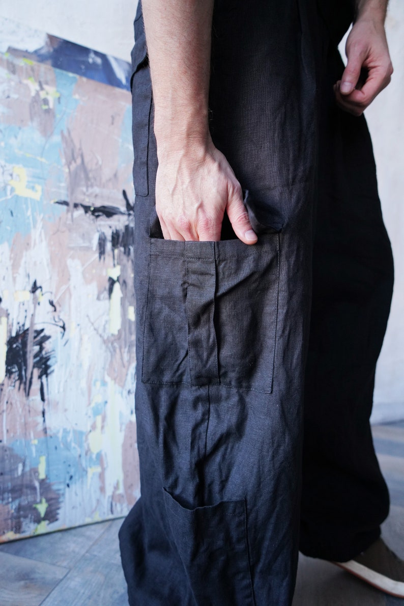 Pu&ograve; includere: Pantaloni in lino grigio scuro con ampie tasche cargo. I pantaloni hanno una vestibilit&agrave; rilassata e uno stile casual. Il tessuto sembra leggero e traspirante, adatto alle temperature pi&ugrave; calde. Una mano &egrave; in tasca.