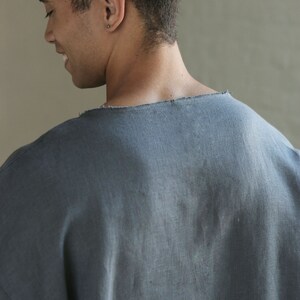 May include: A person wearing a dark gray, loose-fitting, linen shirt with a raw edge neckline.