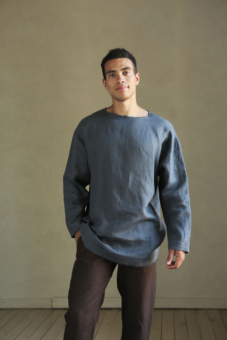 May include: A person wearing a long-sleeved, dark blue linen shirt with a relaxed fit and a round neckline. The shirt is tucked into brown pants.