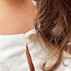 May include: A white linen shirt with a wooden button at the back of the neck.