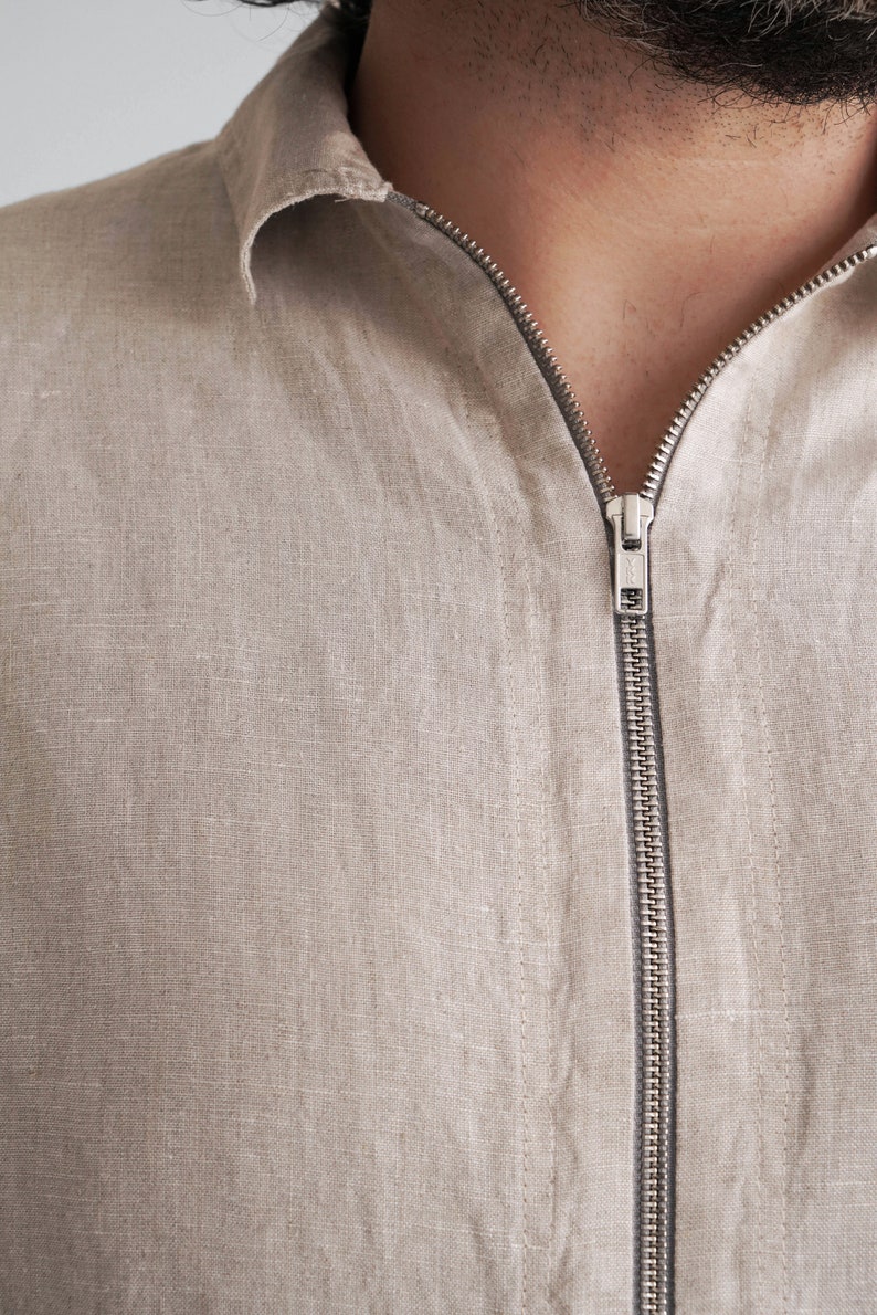 Puede incluir: Una camisa de lino beige con cierre de cremallera. La cremallera es plateada y tiene una peque&ntilde;a leng&uuml;eta de metal.
