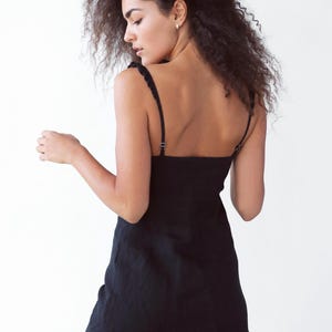 May include: A woman wearing a black, sleeveless mini dress with a square neckline. The dress has a simple, casual style.
