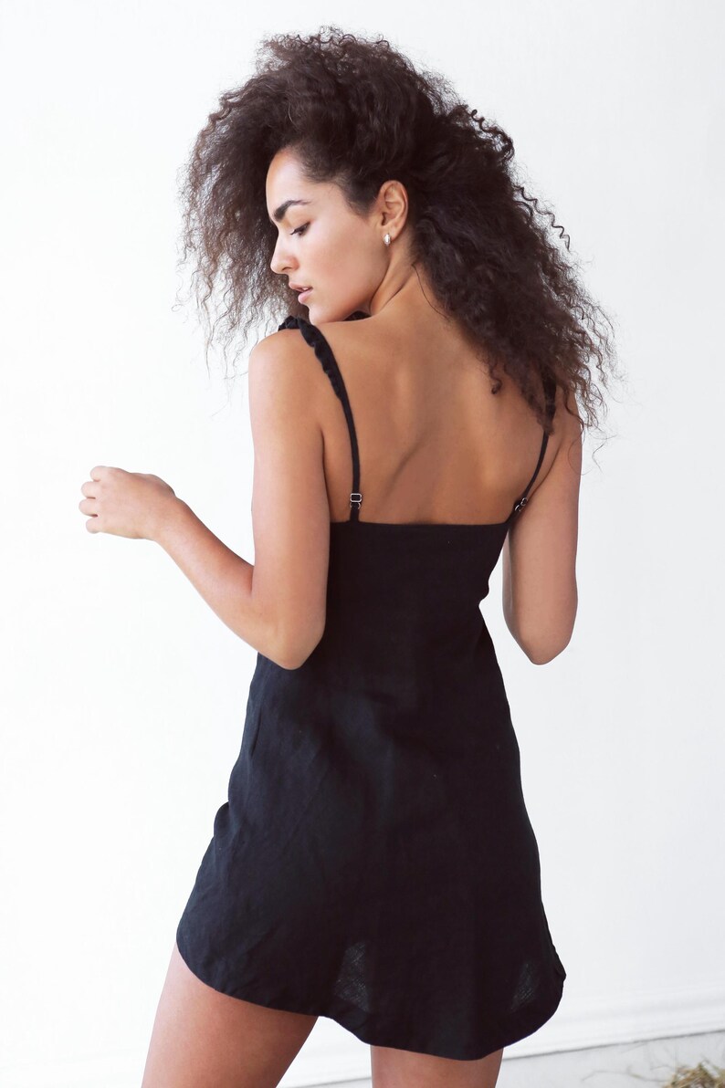 May include: A woman wearing a black, sleeveless mini dress with a square neckline. The dress has a simple, casual style.