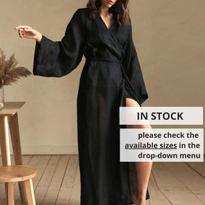 May include: A long, black wrap dress with wide sleeves and a high slit. The dress is tied at the waist and worn by a person. The image includes text that says "IN STOCK" and "please check the available sizes in the drop-down menu."