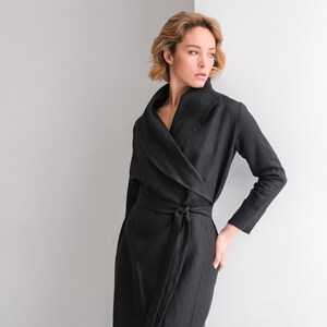 May include: A black linen wrap dress with a long sleeve and a wide collar. The dress has a tie belt at the waist.
