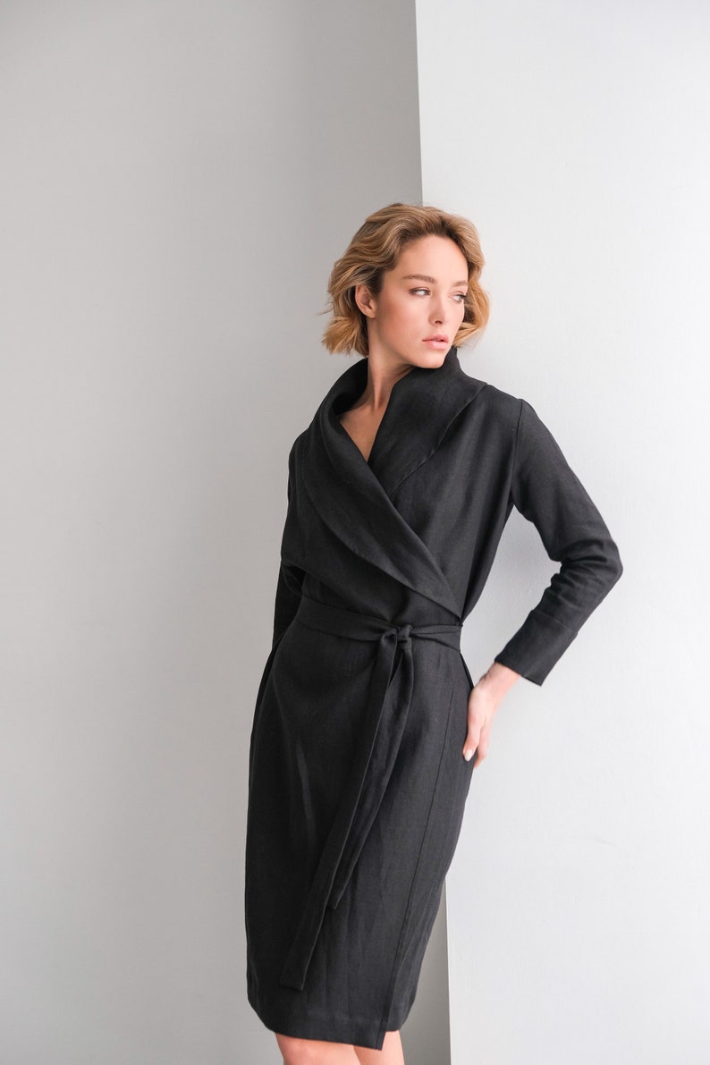 May include: A black linen wrap dress with a long sleeve and a wide collar. The dress has a tie belt at the waist.