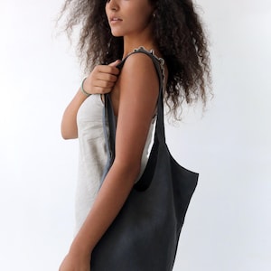 May include: A woman wearing a light grey dress holds a dark grey linen tote bag with a single strap.