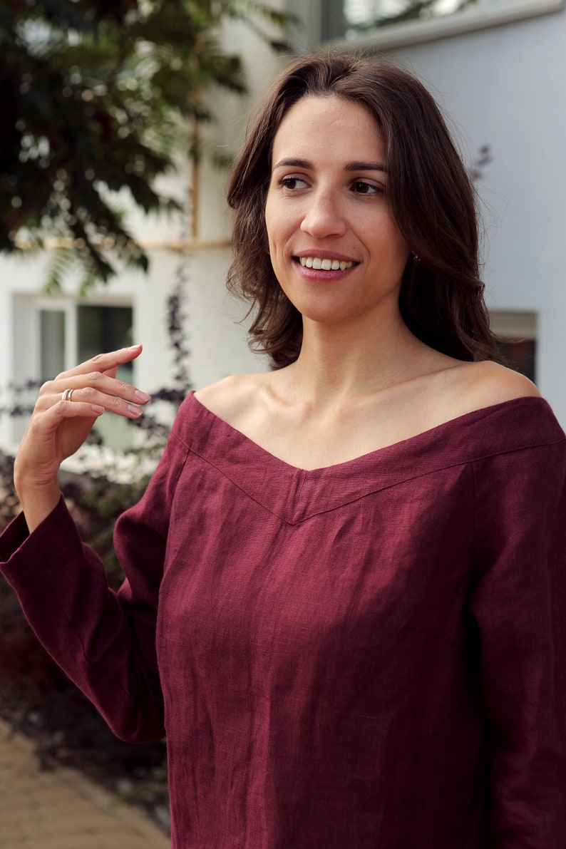 May include: A woman wearing a maroon off-the-shoulder linen top with long sleeves.