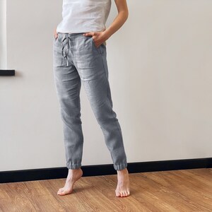 Op de afbeelding: Grijze linnen broek met een trekkoord in de taille en getailleerde pijpen. De broek is losjes gesneden en comfortabel.