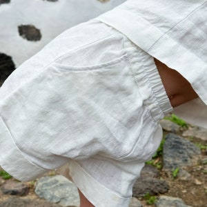 May include: White linen shorts with a single pocket on the back. The shorts have a drawstring waist and are made of a lightweight fabric.