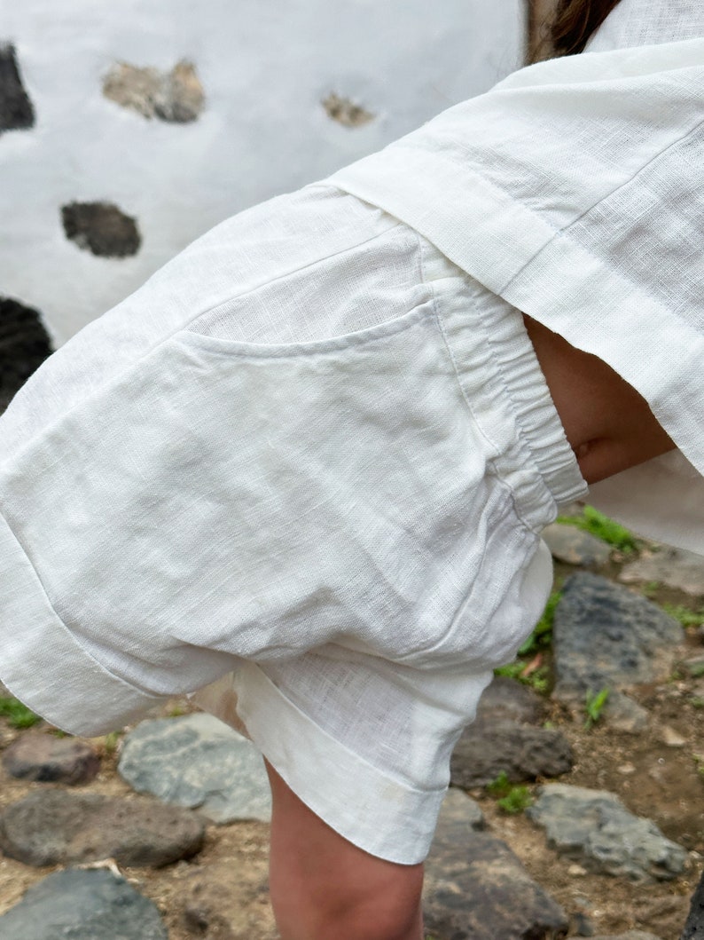 May include: White linen shorts with a single pocket on the back. The shorts have a drawstring waist and are made of a lightweight fabric.