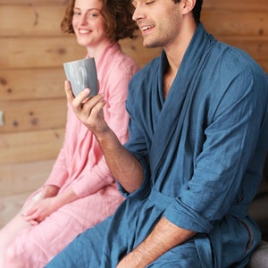 Pode incluir: Um casal com roup&otilde;es combinando azul e rosa, sentado em um sof&aacute;, com o homem segurando uma caneca cinza.