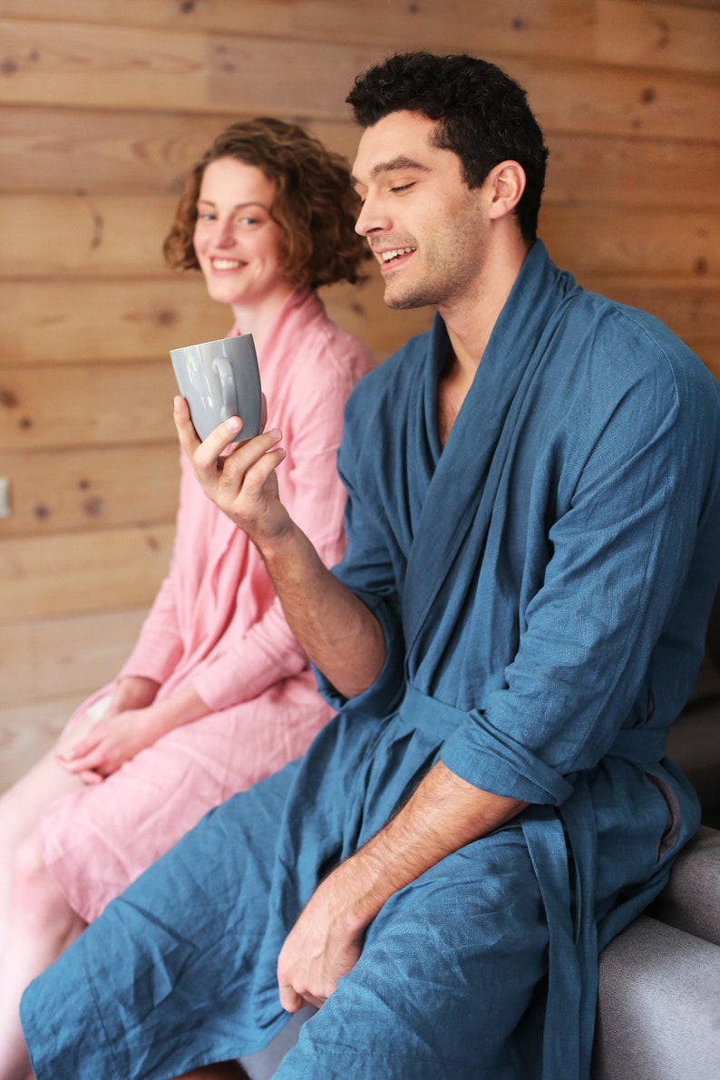 Pode incluir: Um casal com roup&otilde;es combinando azul e rosa, sentado em um sof&aacute;, com o homem segurando uma caneca cinza.