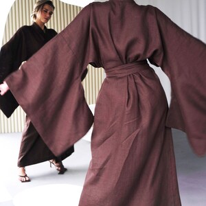 May include: A long, brown linen robe with wide sleeves and a sash tie at the waist. The robe is worn by a person standing in front of a mirror.