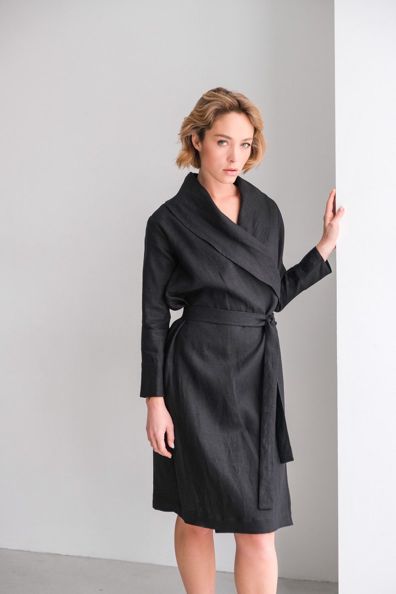 May include: A black linen wrap dress with a long sleeve and a tie belt. The dress has a deep V-neckline and a relaxed fit.