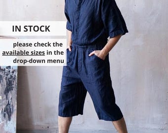 May include: A dark blue linen jumpsuit featuring a mandarin collar, short sleeves, an elasticated waistband, and two front pockets. The text IN STOCK please check the available sizes in the drop-down menu is visible on the left side of the image.