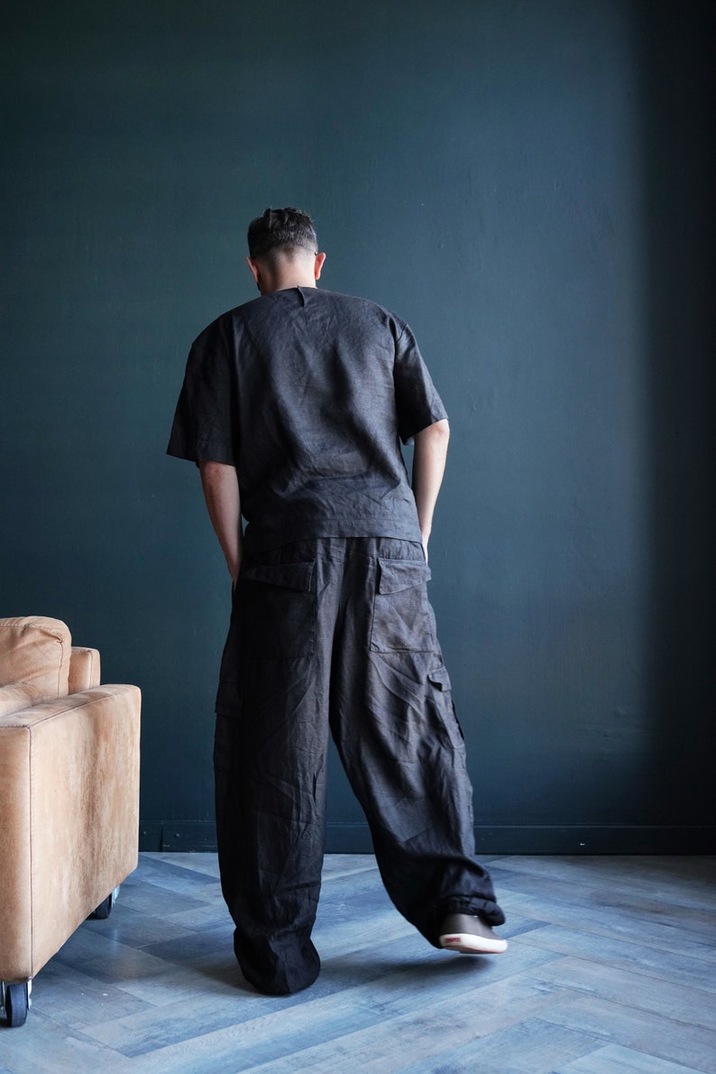 Pu&ograve; includere: Un completo in lino grigio scuro, composto da un top a maniche corte e pantaloni cargo a gamba larga. I pantaloni hanno ampie tasche laterali. L'outfit &egrave; indossato con scarpe da ginnastica scure. Lo sfondo &egrave; un muro blu scuro.