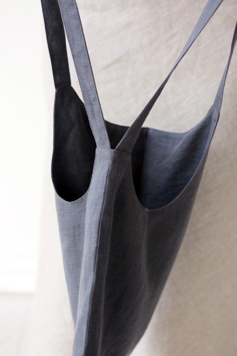 May include: A grey linen tote bag with two long straps. The straps are crossed at the top of the bag.